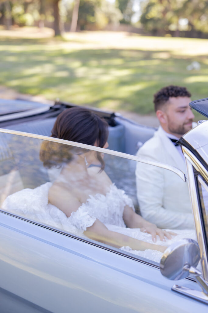 Bride and groom driving in a vintage baby blue Mustang.