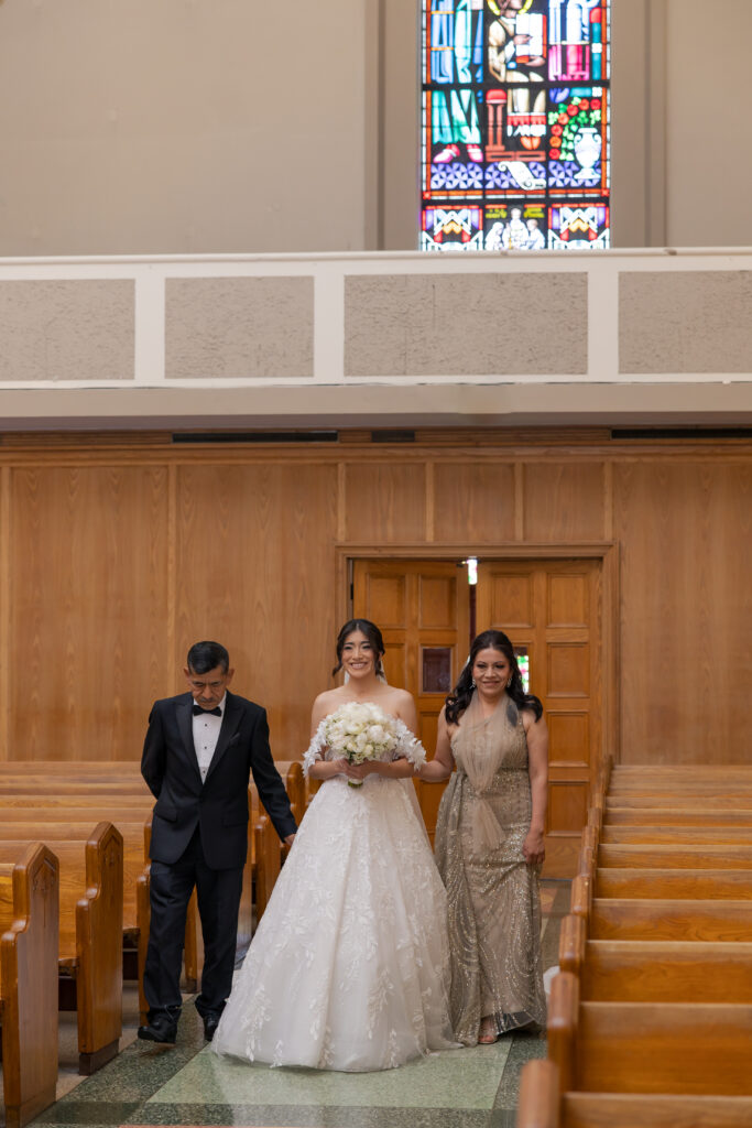 Bride walking down the aisle with her parents at Saint Emydius church in Los Angeles.