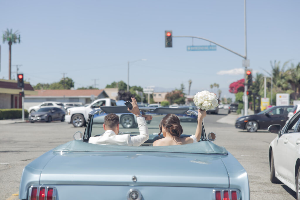 Bride and groom driving away in a classic baby blue Mustang after their Los Angeles wedding ceremony.