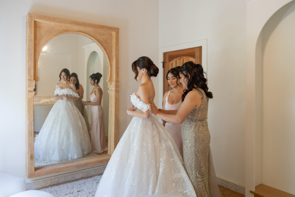Bride's mom and sister helping her put on her wedding dress in the Grand Gimeno bridal suite.