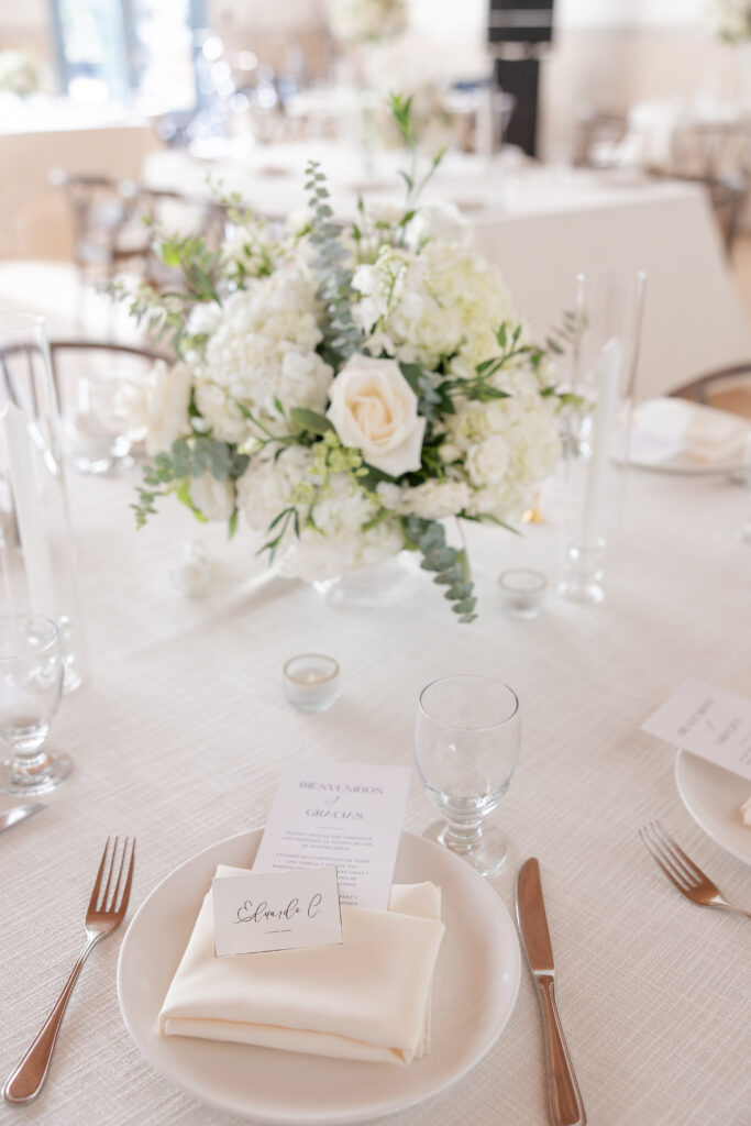 Elegant white wedding table place setting with a floral centerpiece.