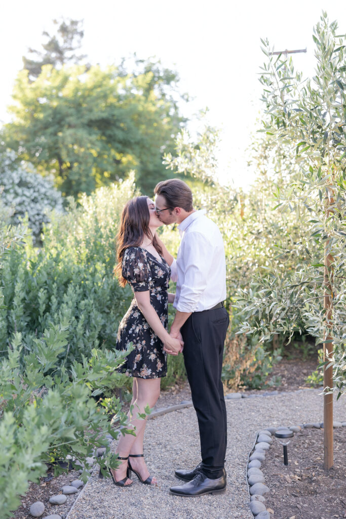 Couple kissing on a gravel walkway surrounded by olive trees and lavender shrubs at Olive + Lavender Farms. 