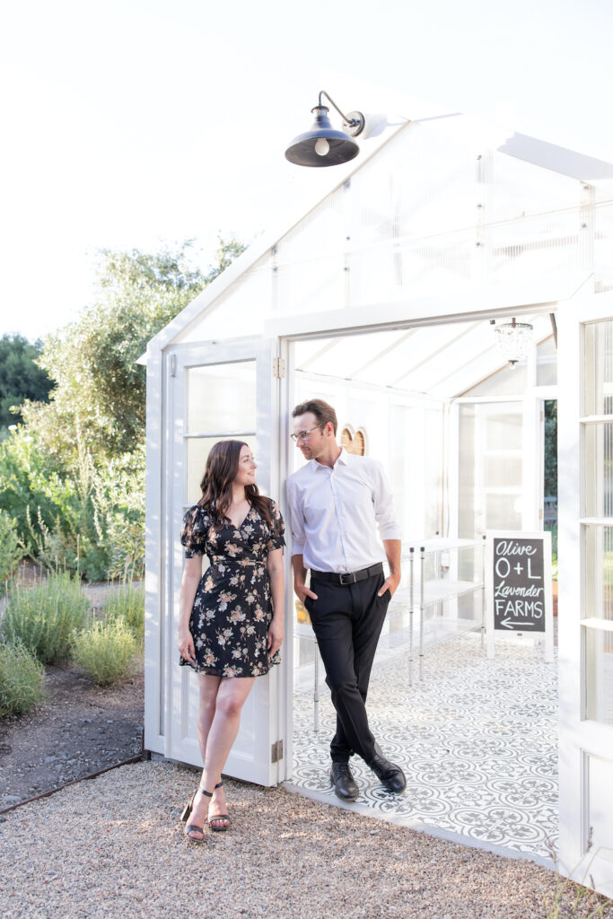 Couple posing next to the Olive + Lavender Farms greenhouse for their engagement session. 