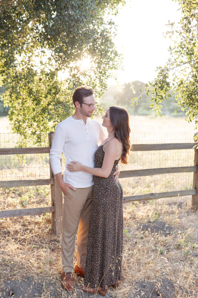 Couple standing in front of a wooden fence at Olive + Lavender Farms for their engagement session. 