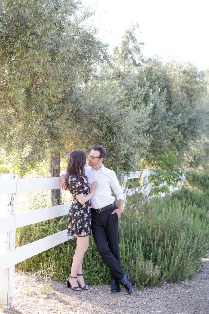Couple posing next to a lavender shrub and olive trees at Olive + Lavender Farms. 