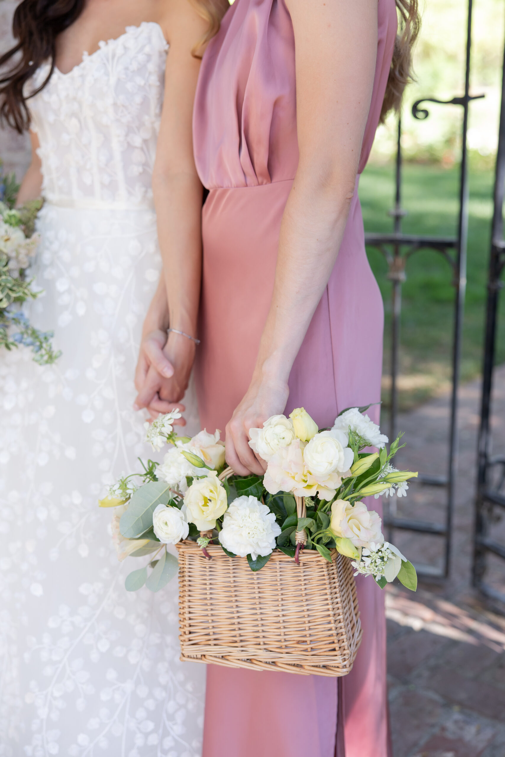 Close up of a bride and her bridesmaid holding a wicker basket brimming with flowers. 