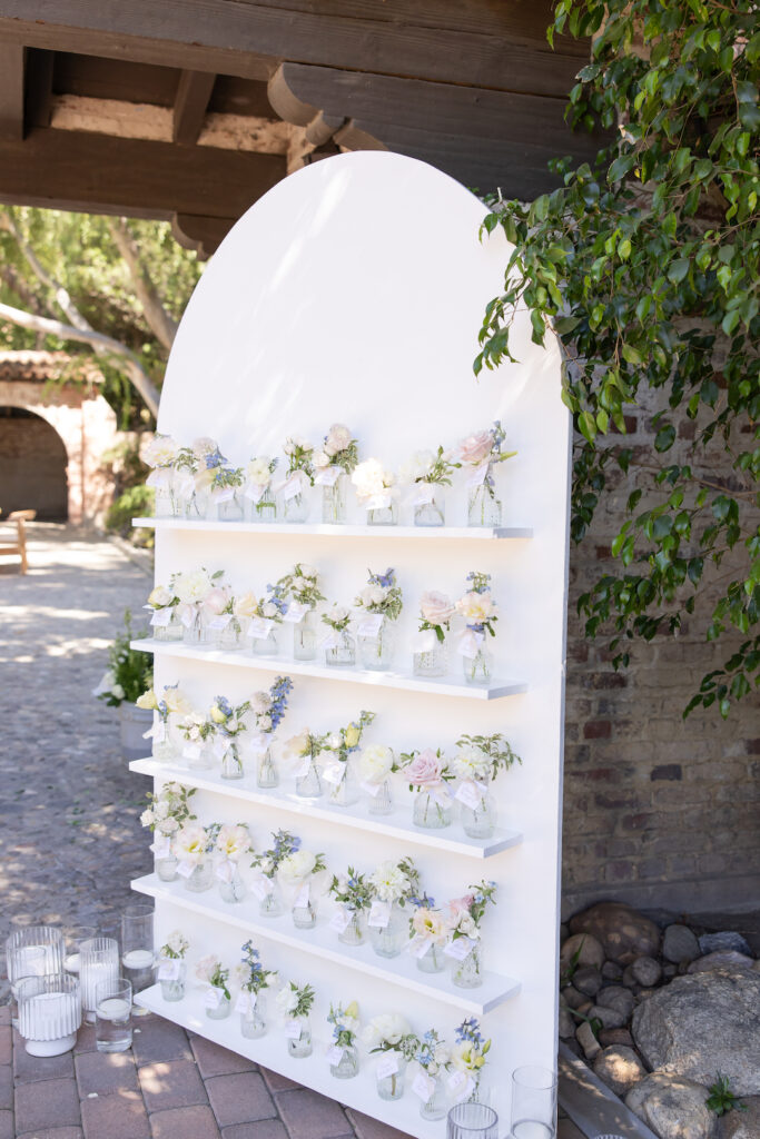 Six-foot pastel seating chart display with whimsical floral arrangements in  bud vases. 
