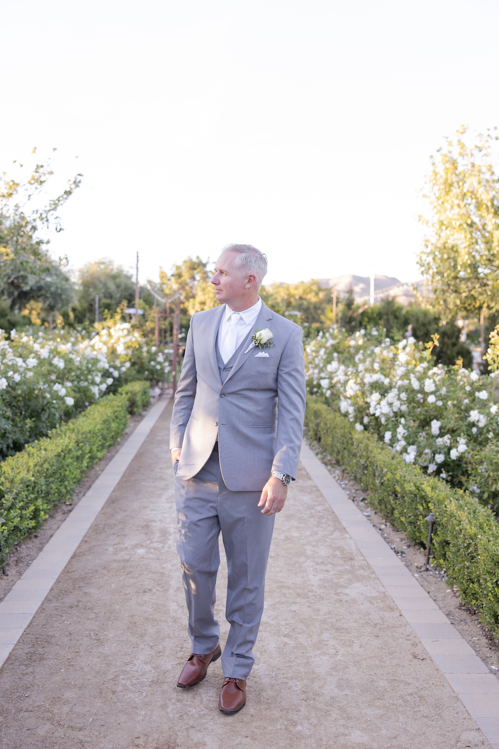 Groom walking a floral lined garden path at Tuscan Rose Ranch.
