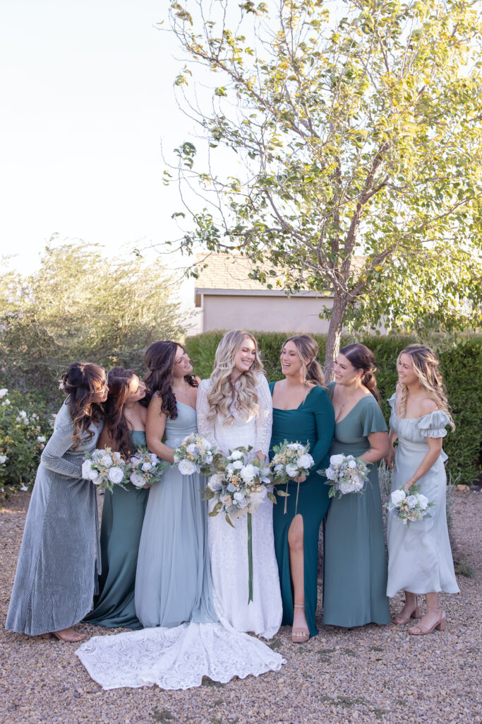 Bride and bridesmaid candid group photo with varying shades of sage green bridesmaid dresses. 