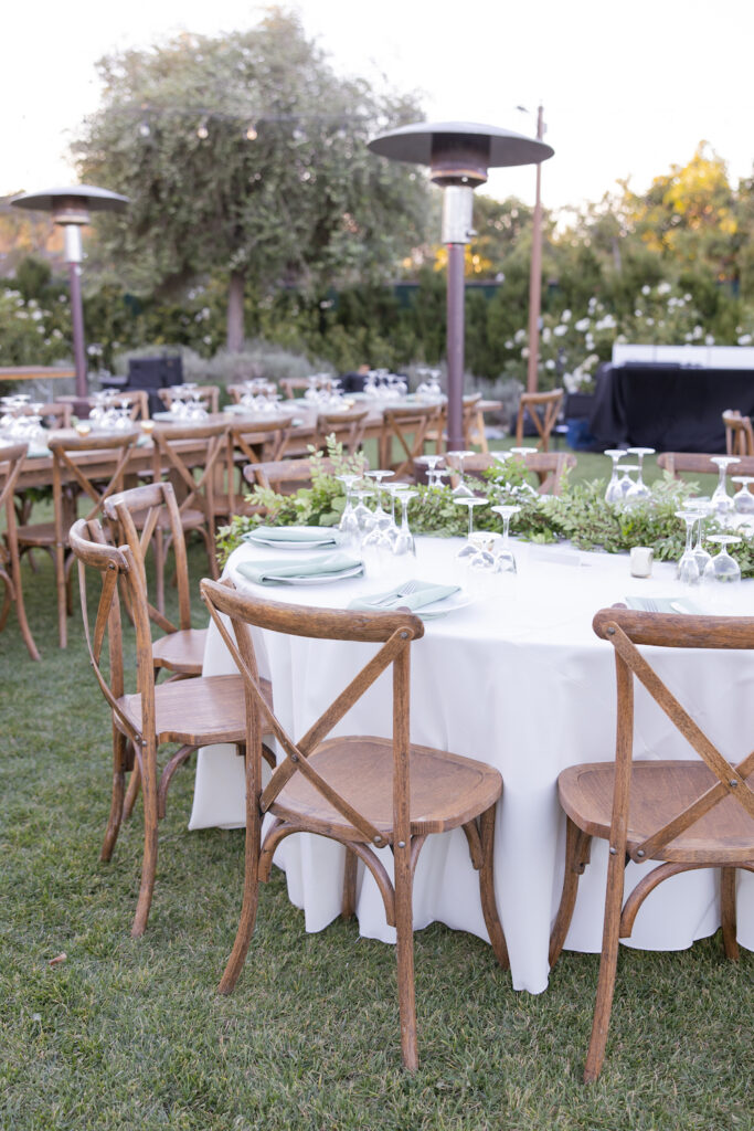 White and greenery wedding reception table with wooden chairs at Tuscan Rose Ranch.